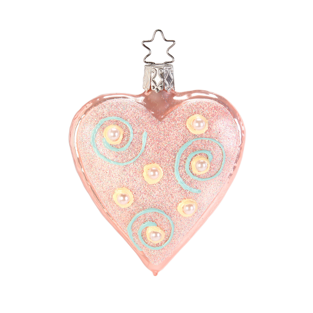Heart-shaped ornament with pink glitter, pearl-like beads, and blue swirls on a white background.