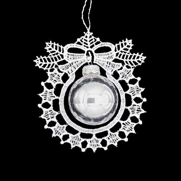 Decorative white lace ornament in the shape of a wreath with a bow and a silver glass ball in the center on a black background.