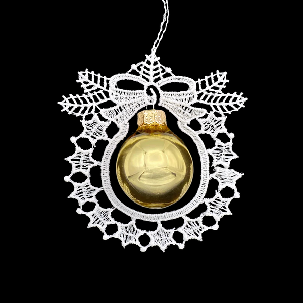 Decorative white lace ornament in the shape of a wreath with a bow and a gold glass ball in the center on a black background.