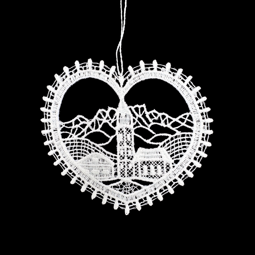 Decorative white heart-shaped lace ornament with a scenic church and landscape design in the middle, on a black background