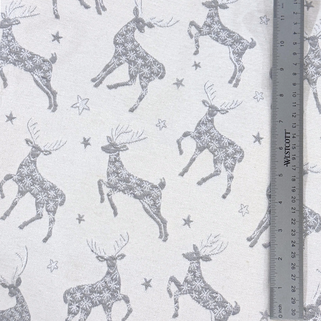 Close up pattern of stags and stars in a dark silvery gray on a light gray background with a ruler to show scale.
