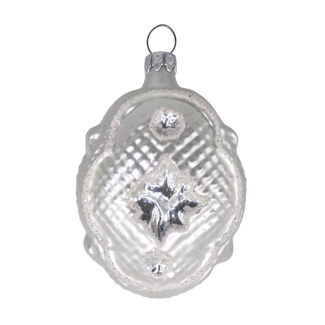 Decorative glass ornament in the shape of a Victorian pillow with scalloped edges and a star design in the center on a white background
