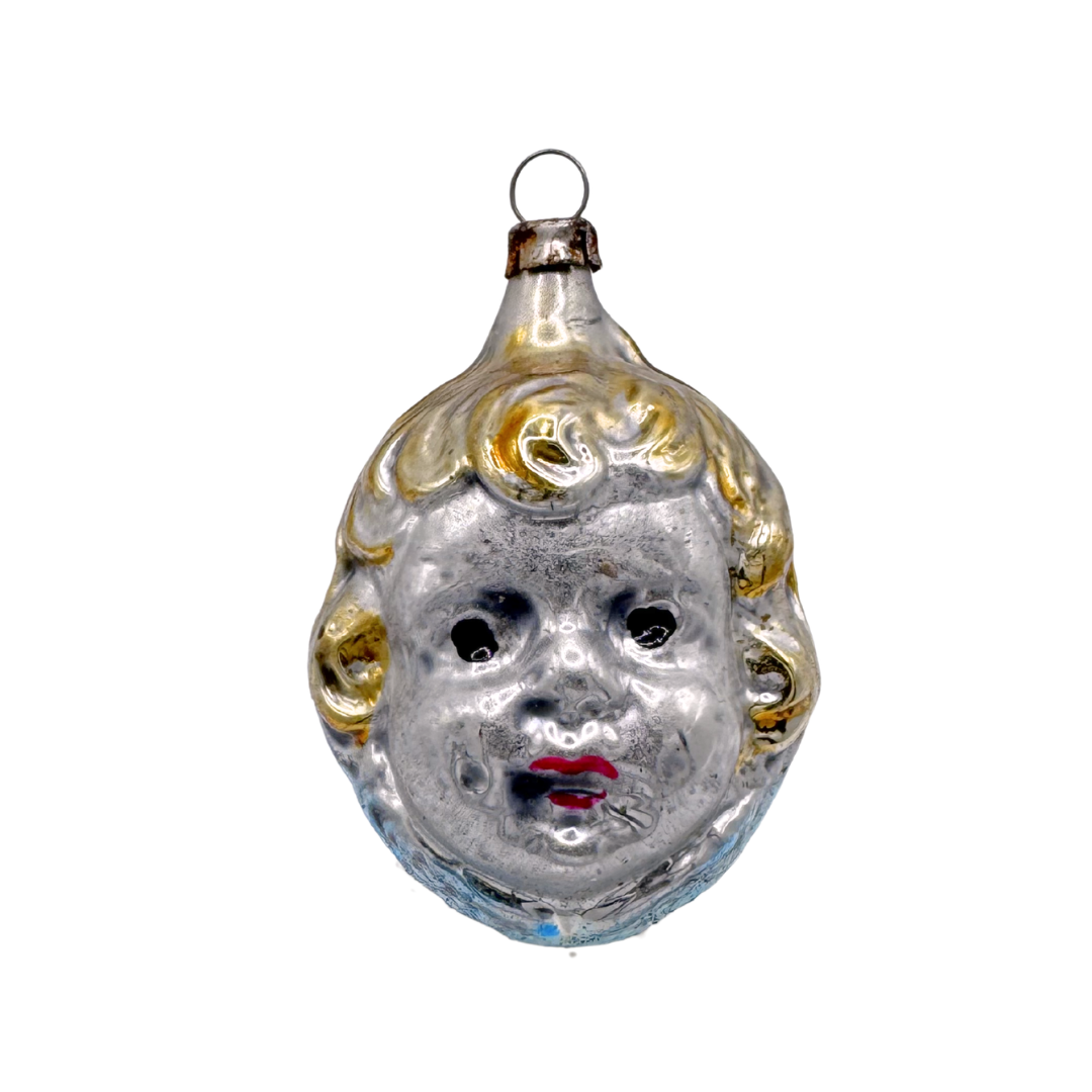 Decorative glass ornament shaped like a child's face in silver with yellow hair and red lips, antiquing all over to give a vintage feel.