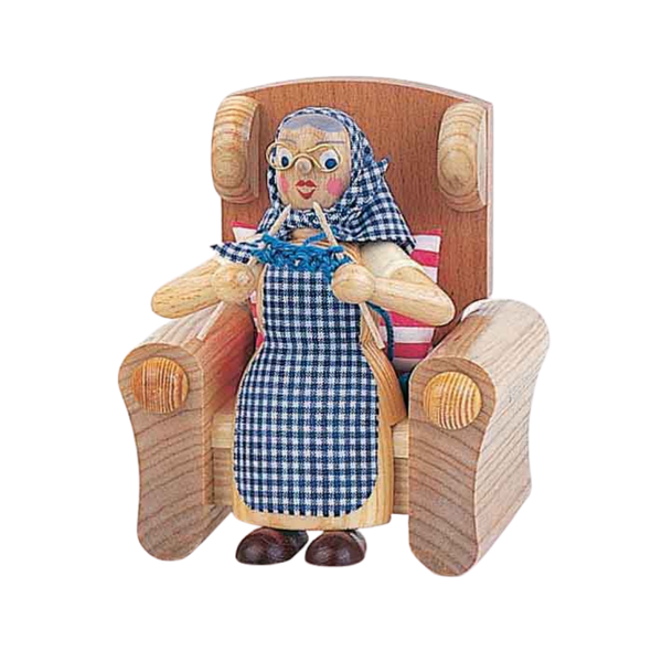 Wooden figurine of a woman sitting in an arm chair, wearing a checkered dress and headscarf, knitting.