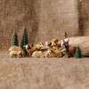 A collection of hand-carved wooden miniature figures depicting a sheep herd with a shepherd, trees, and a natural backdrop.