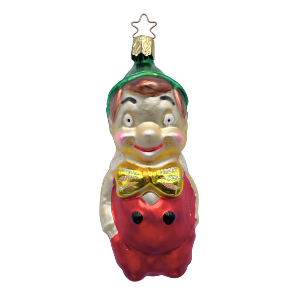 A glass ornament depicting a stylized version of Pinocchio, with a green hat and a red and gold coat, designed by Inge Glas of Germany.