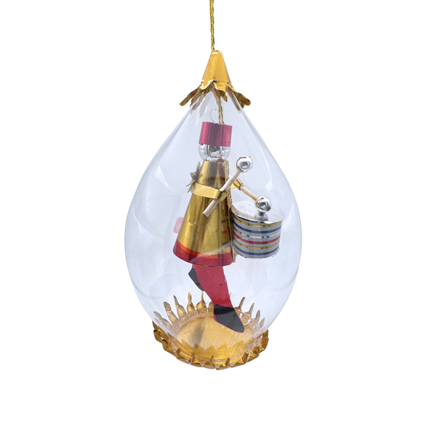 A clear teardrop-shaped hanging ornament containing a small gold-and-red toy soldier figure with a drum, suspended by a gold string against a white background.