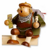 A handcrafted wooden incense smoker in the shape of a cartoonish tourist with a map and a backpack. The smoker is primarily green with brown accents for the clothing and a wooden base.